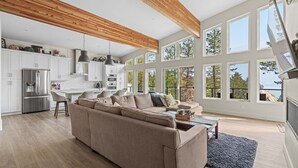 A spacious living area with a large sofa, a dining table, and a kitchen with white cabinets and a wooden ceiling.