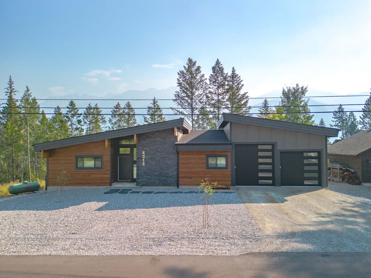A modern two-story house with a stone facade, a garage, and a gravel driveway.