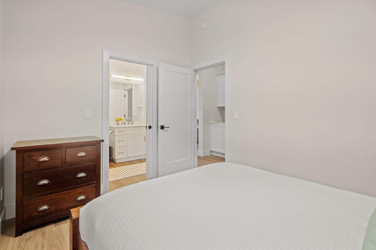 A bedroom with a bed, a dresser, and a bathroom visible through an open door.