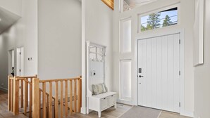A hallway with a wooden staircase, a white bench, a coat rack, and a white door.
