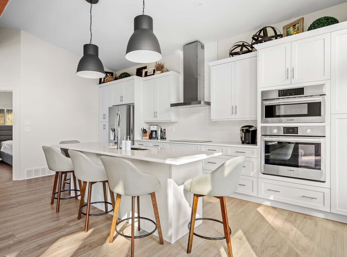 A modern kitchen with white cabinetry, a central island with bar stools, and built-in appliances including a Bosch oven.
