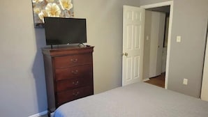 Une chambre à coucher comprenant un lit, une commode, un téléviseur posé sur la commode et une porte donnant sur une autre pièce.