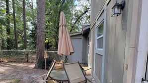 Une terrasse extérieure avec une table et des chaises à plateau en verre, un parasol beige et une clôture en bois.