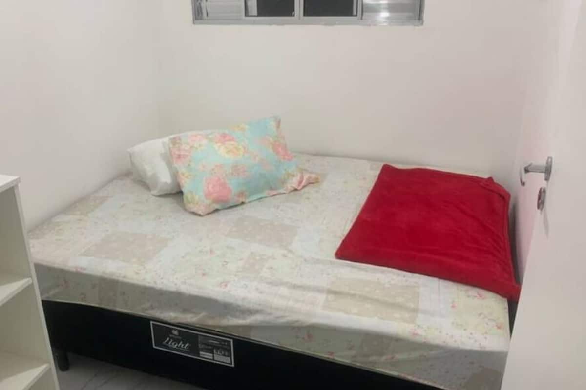 A small, single-bed room with a mattress, a red blanket, and a floral pillow.