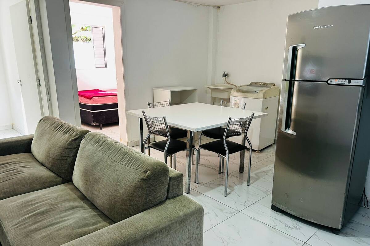 A compact living space with a sofa, dining table, chairs, a kitchenette, and a refrigerator.