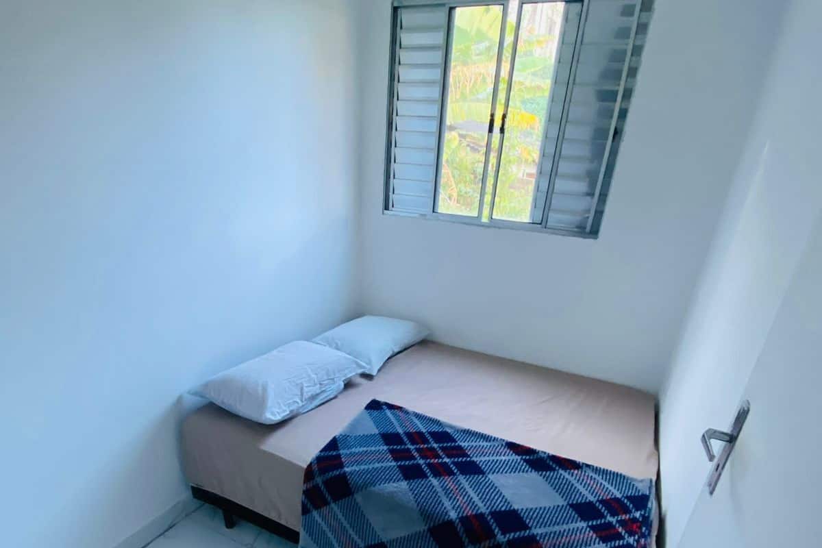 A small, single-bed room with a window, white walls, and a tiled floor.