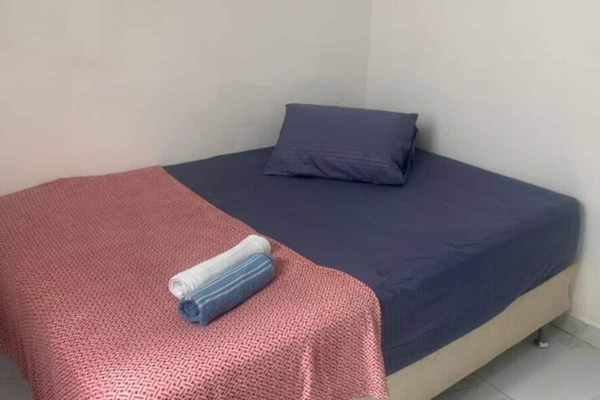 A single bed with a red patterned bedspread and a blue pillow.