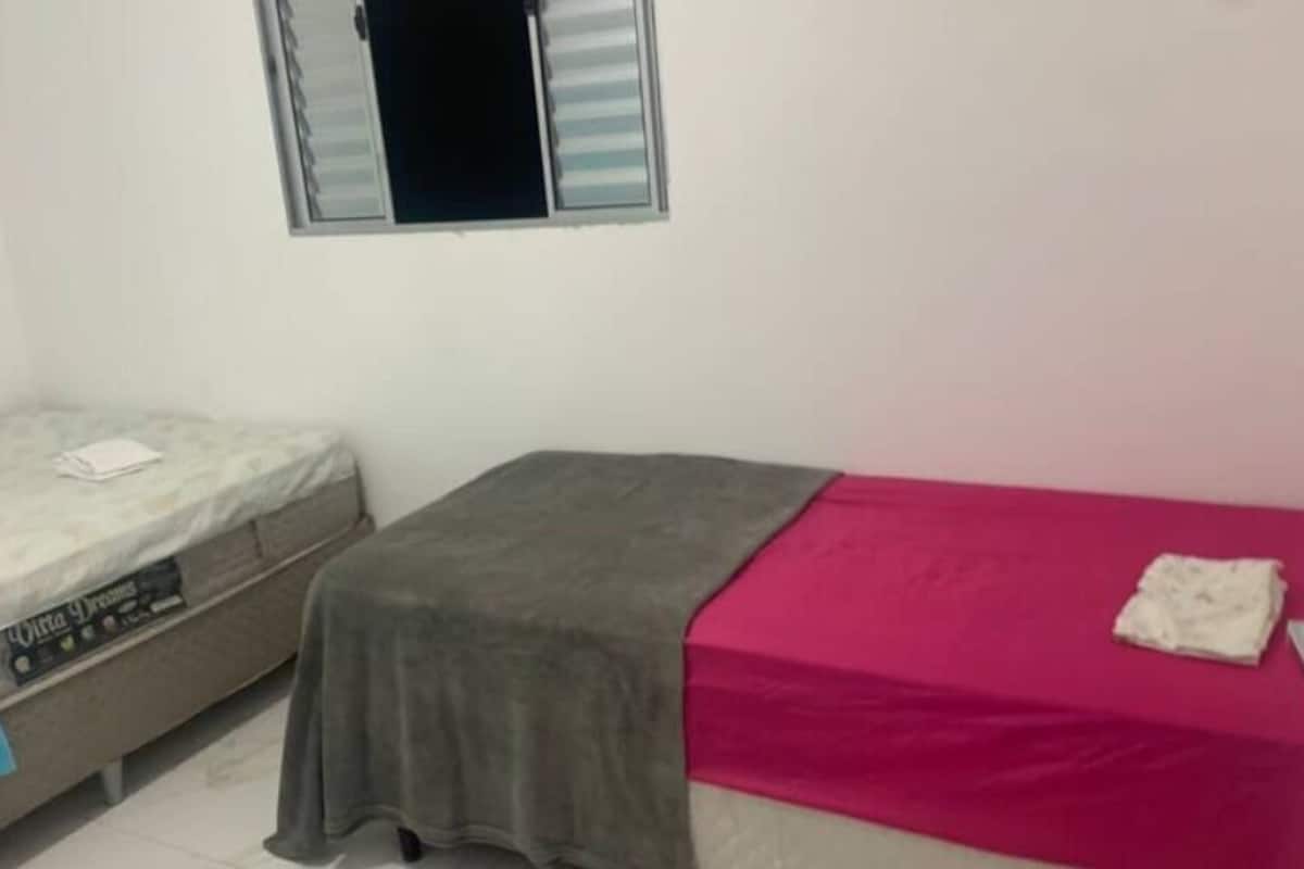 A small room with two beds, one with a blue blanket and the other with a pink blanket.