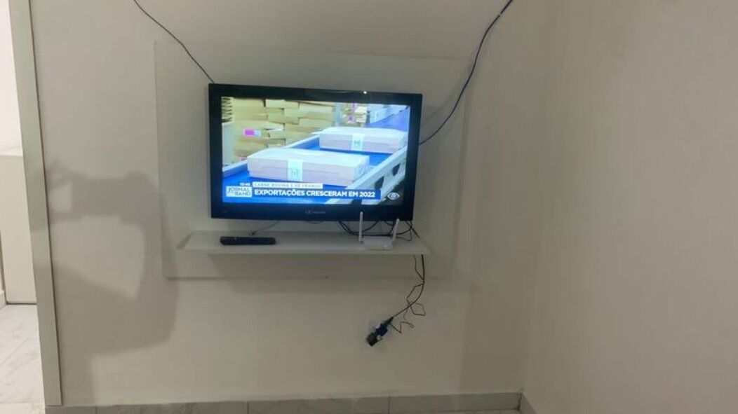 Een televisie bevestigd aan een muur, met een afstandsbediening op een voet eronder.