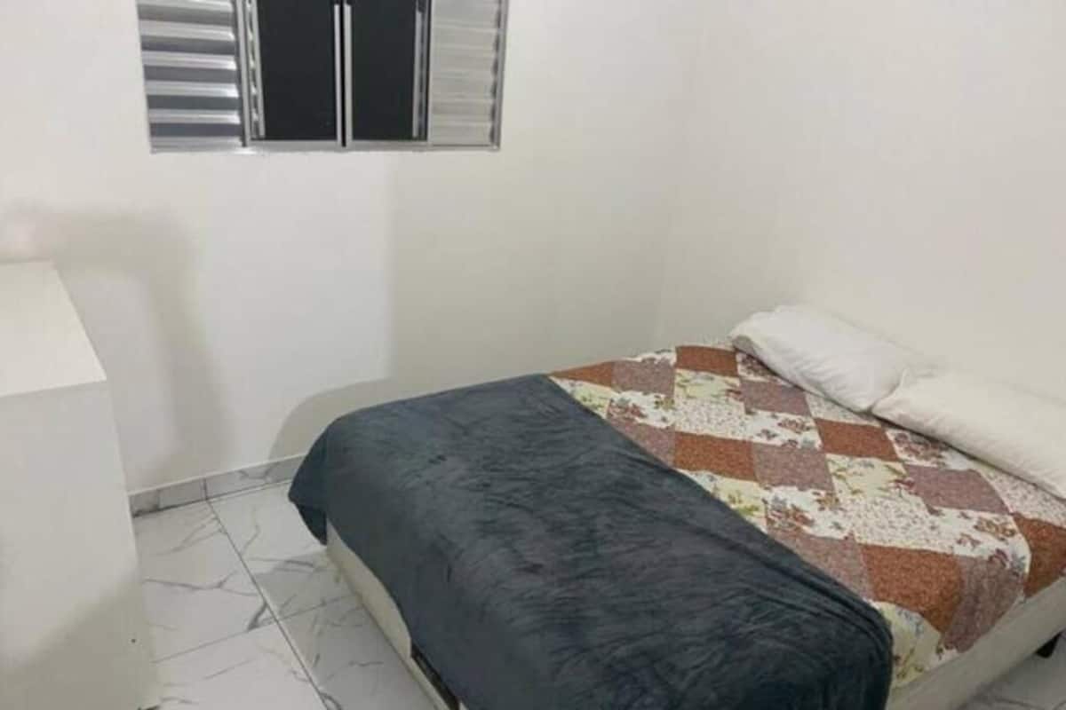 A bedroom with a bed, a nightstand, a window with blinds, and a patterned bedspread.