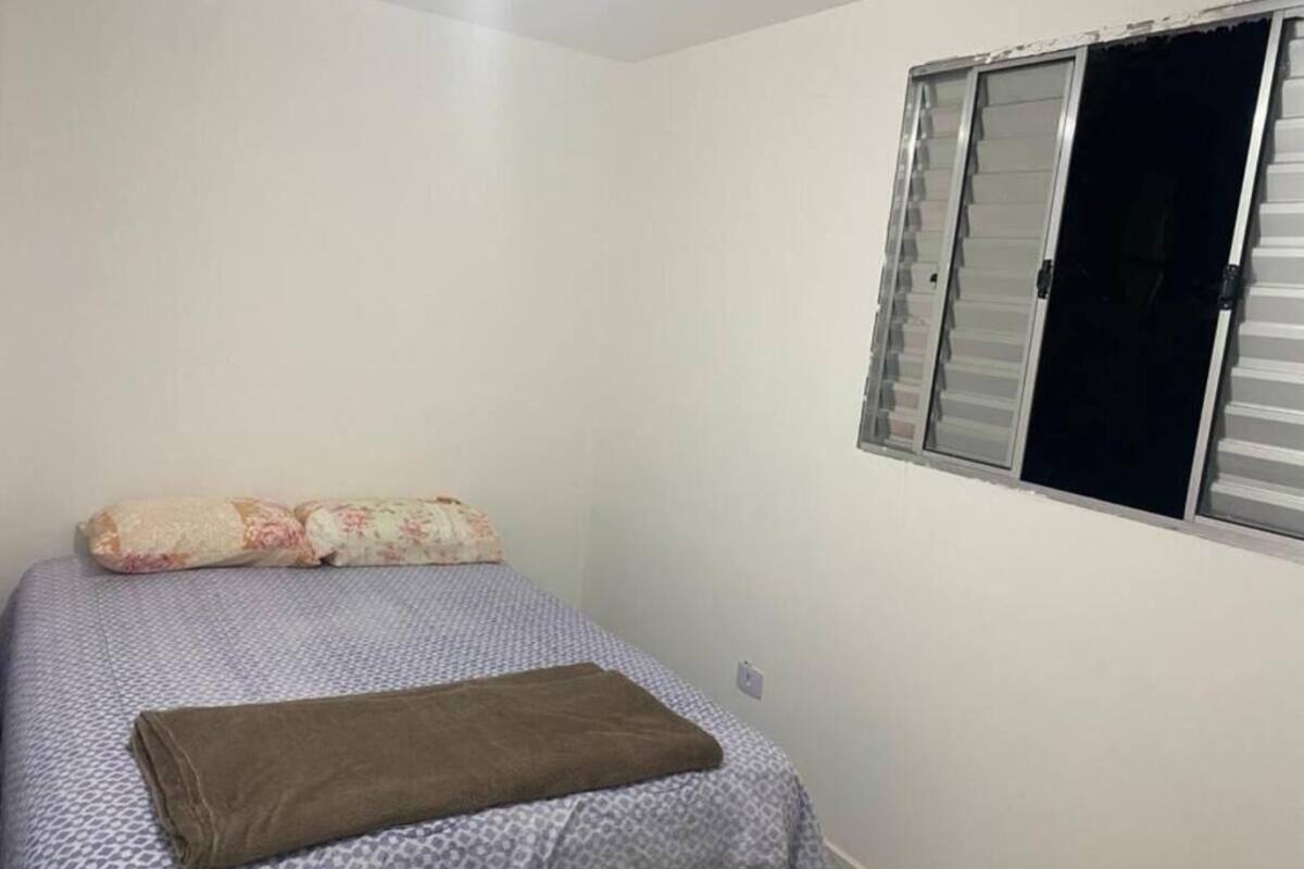 A bedroom with a bed, a window with blinds, and a wall socket.