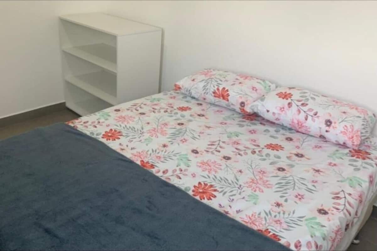 A bedroom with a bed, floral bedding, a grey blanket, and a white shelving unit.