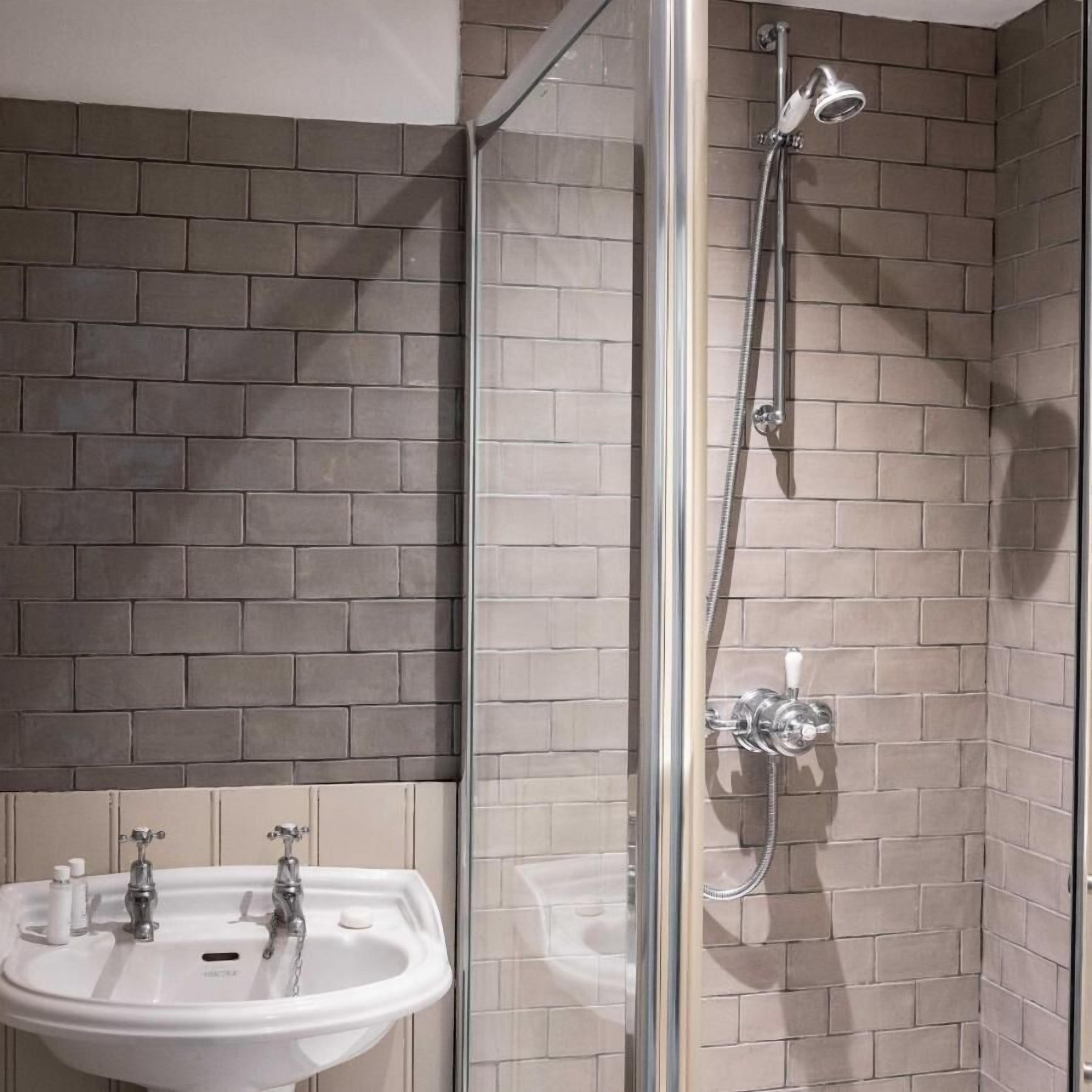 A bathroom with a glass-enclosed shower, a white sink, and a tiled wall.