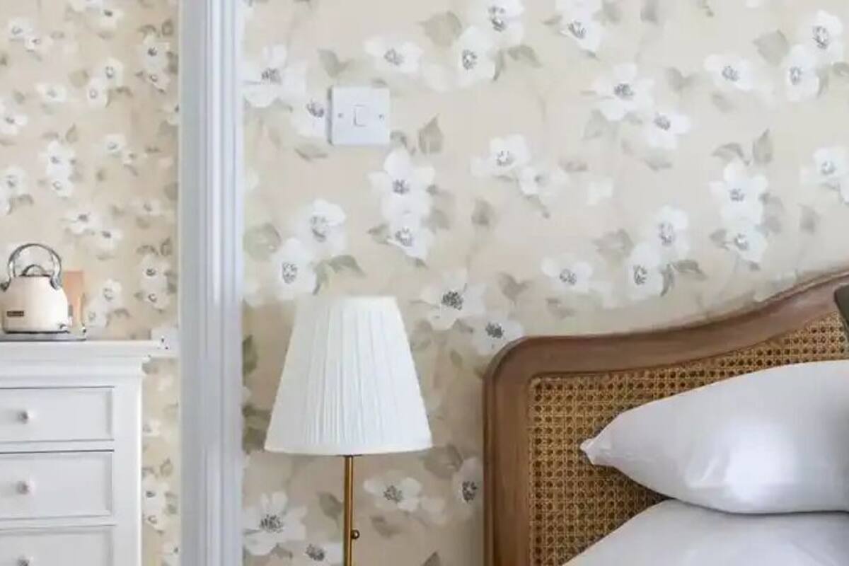 Un dormitorio con papel tapiz floral, cabecera de madera, dos almohadas, una mesita de noche y dos lámparas.