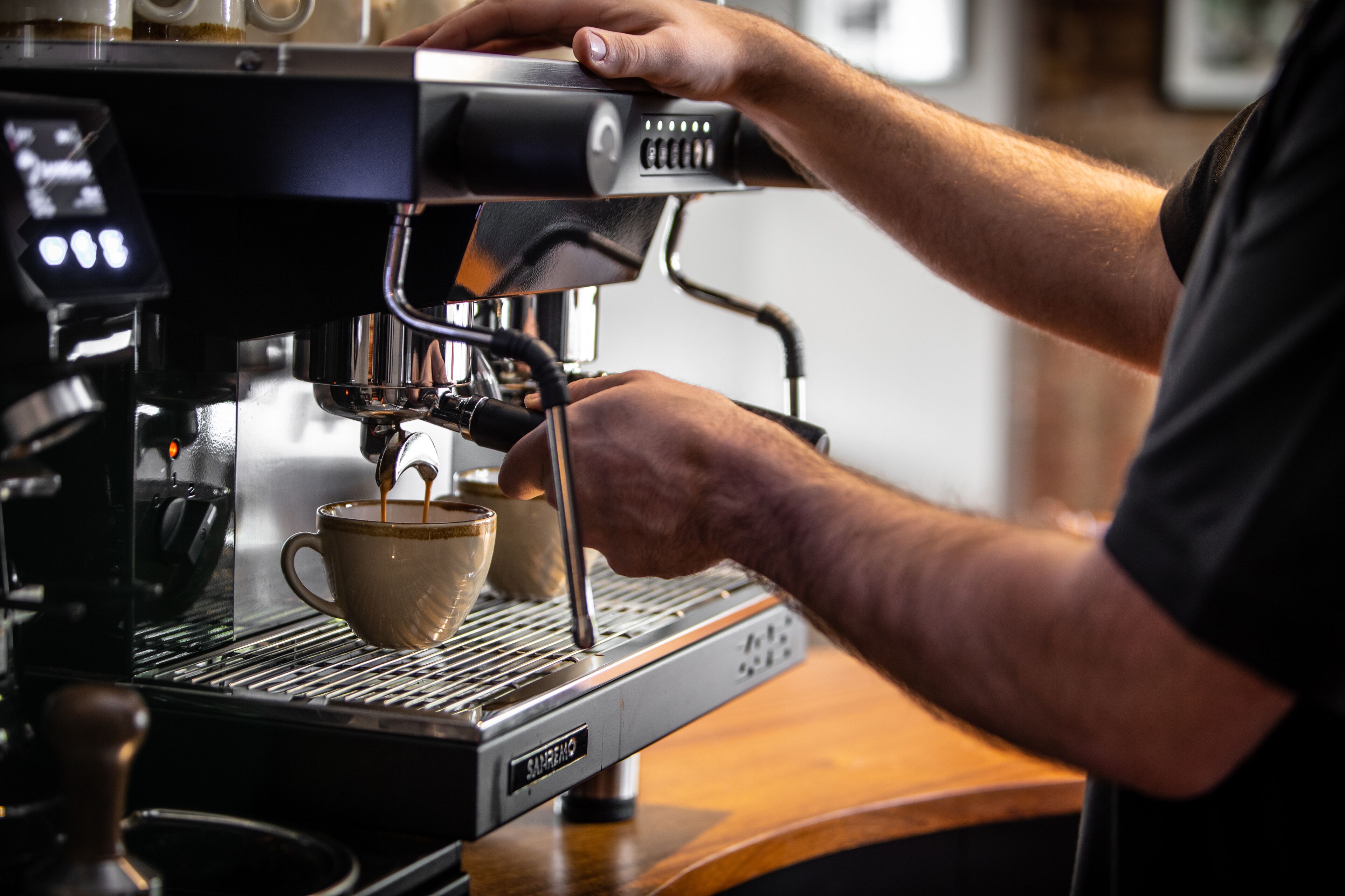 A person operating an espresso machine, with a cup placed under the spout.