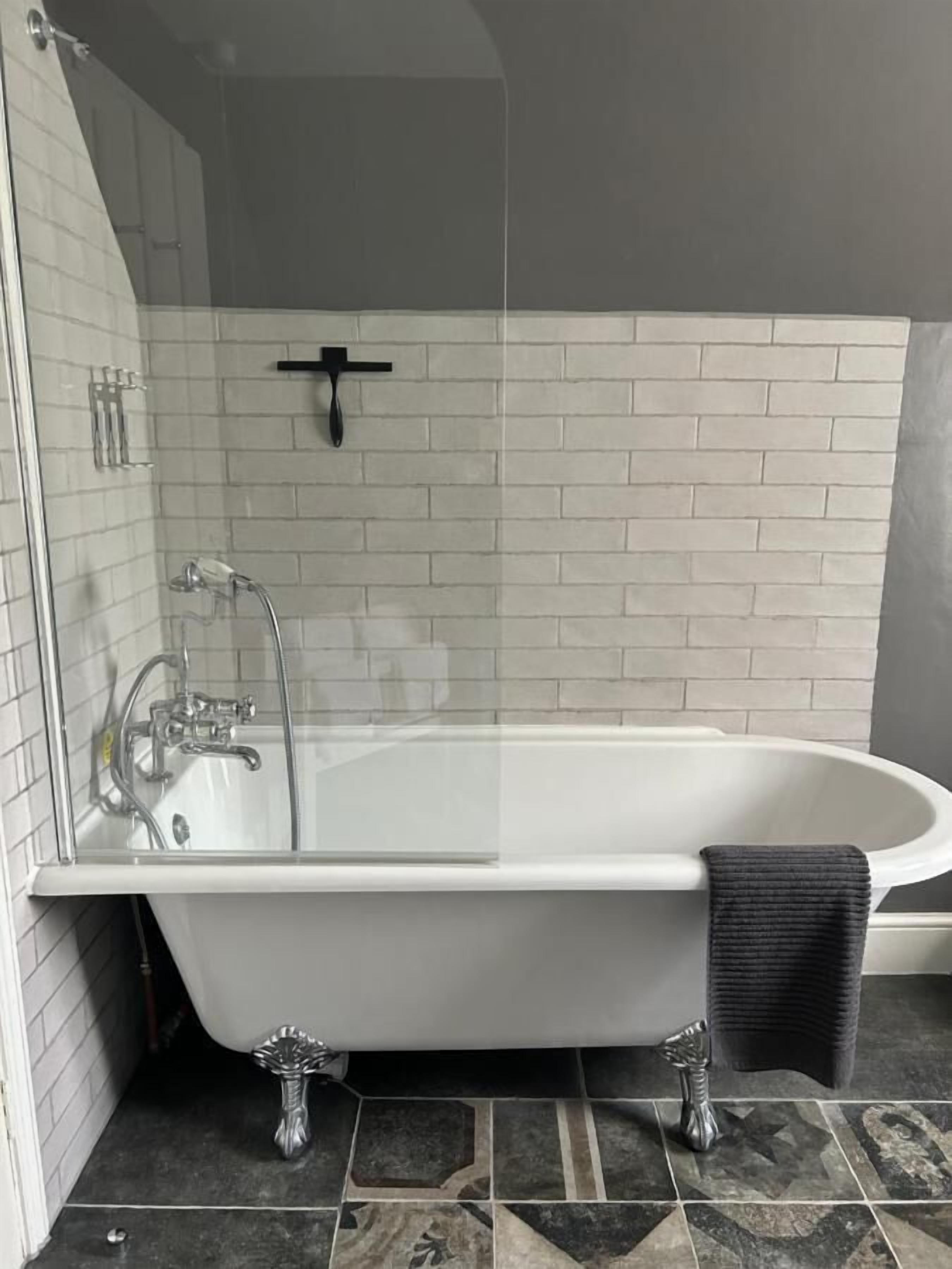 Une salle de bain moderne avec une baignoire sur pieds, une douche à parois de verre et un sol carrelé.