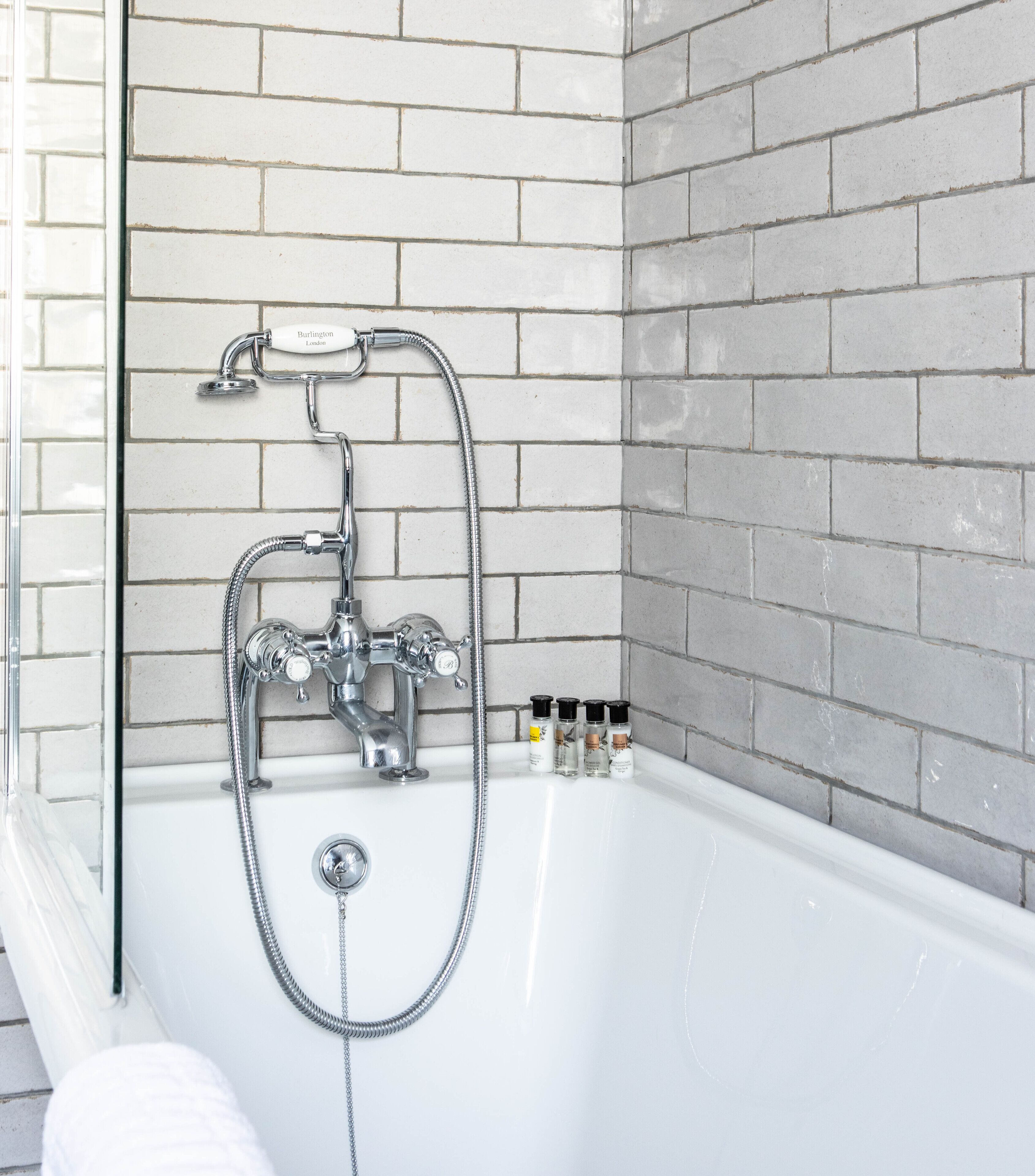 A bathroom with a white bathtub, a chrome showerhead, and a tiled wall.