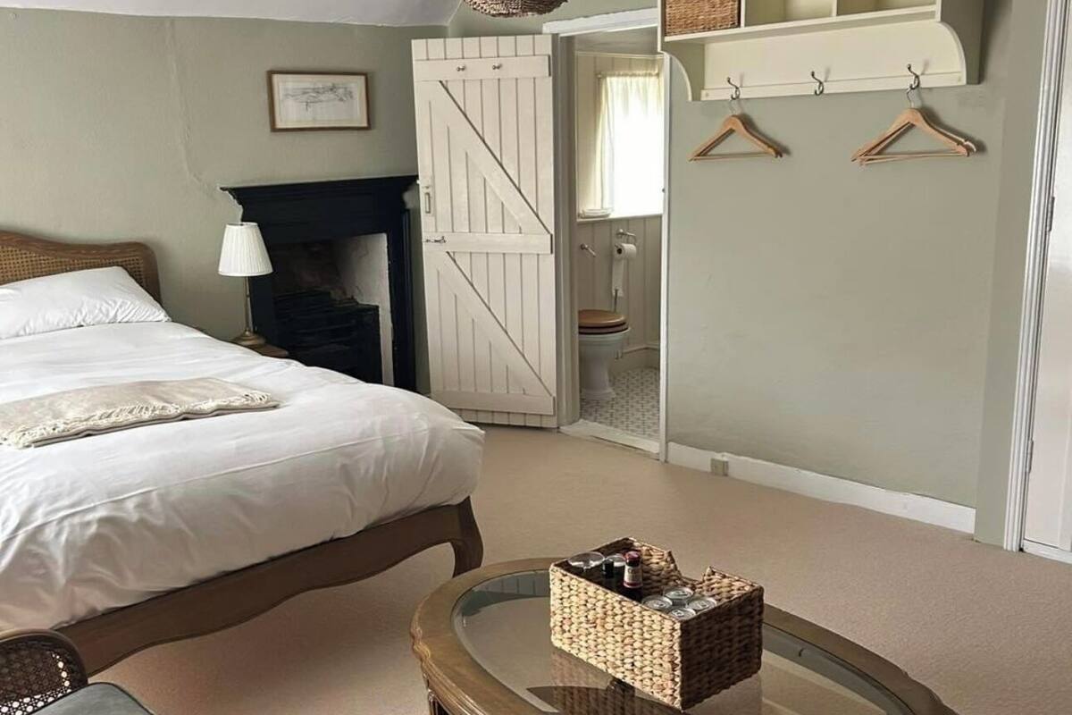 Un dormitorio con cama, una mesita de centro de cristal, una lámpara colgante, un armario y la puerta del baño.