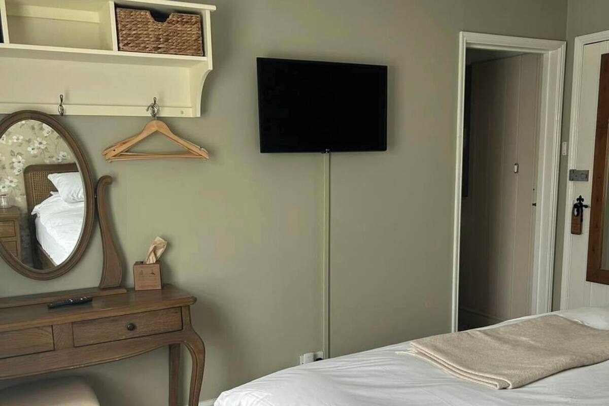 Un dormitorio con cama, cómoda, espejo, televisor y puerta.