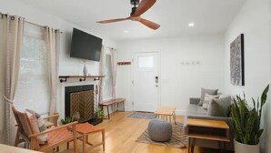A modern living room with a fireplace, ceiling fan, flat-screen TV, and comfortable seating.