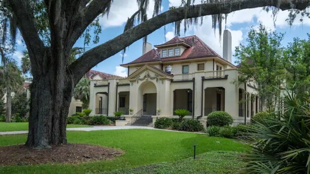 A large, elegant house with a symmetrical facade, multiple entryways, and a well-maintained lawn.