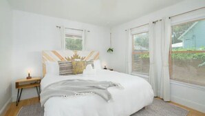 A bedroom with a large bed, a bedside table with a lamp, and a window with blinds.