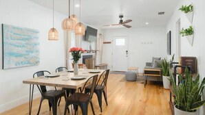 A modern dining area with a wooden table and chairs, pendant lights, and a ceiling fan.