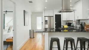 A modern kitchen with stainless steel appliances, a central island with bar stools, and a view into the adjacent bedroom.