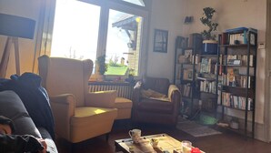 A cozy living room with a large window, a bookshelf, and a comfortable seating area.