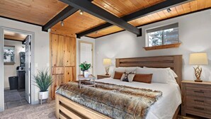 A bedroom with a large bed, wooden headboard, two bedside tables with lamps, a wooden wardrobe, and a plant. - Romantic Lakeview Cabin | Hot Tub + Incredible Views (Divide)