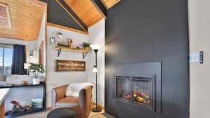A cozy living room with a fireplace, wooden ceiling, and a comfortable chair. - Romantic Lakeview Cabin | Hot Tub + Incredible Views (Divide)