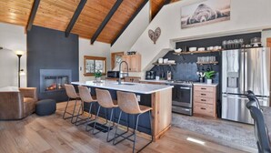 A modern kitchen with a central island, wooden ceiling beams, and a fireplace. - Romantic Lakeview Cabin | Hot Tub + Incredible Views (Divide)
