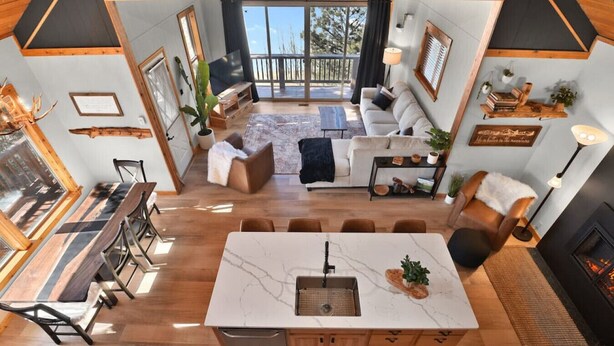 A modern kitchen with a central island, dining area with wooden chairs, a sofa, and a fireplace. - Romantic Lakeview Cabin | Hot Tub + Incredible Views (Divide)
