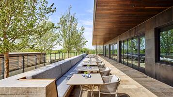 An outdoor dining area with a long bench, tables, and chairs, overlooking a scenic view.