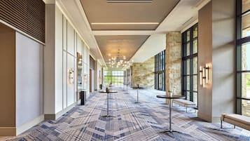 A spacious hallway with patterned carpet, benches, and tables, leading to a large open area with stone walls and large windows.