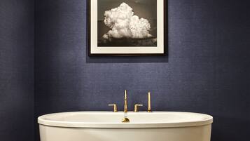 A bathroom with a bathtub, three gold faucets, and a framed picture of a cloud on the wall.