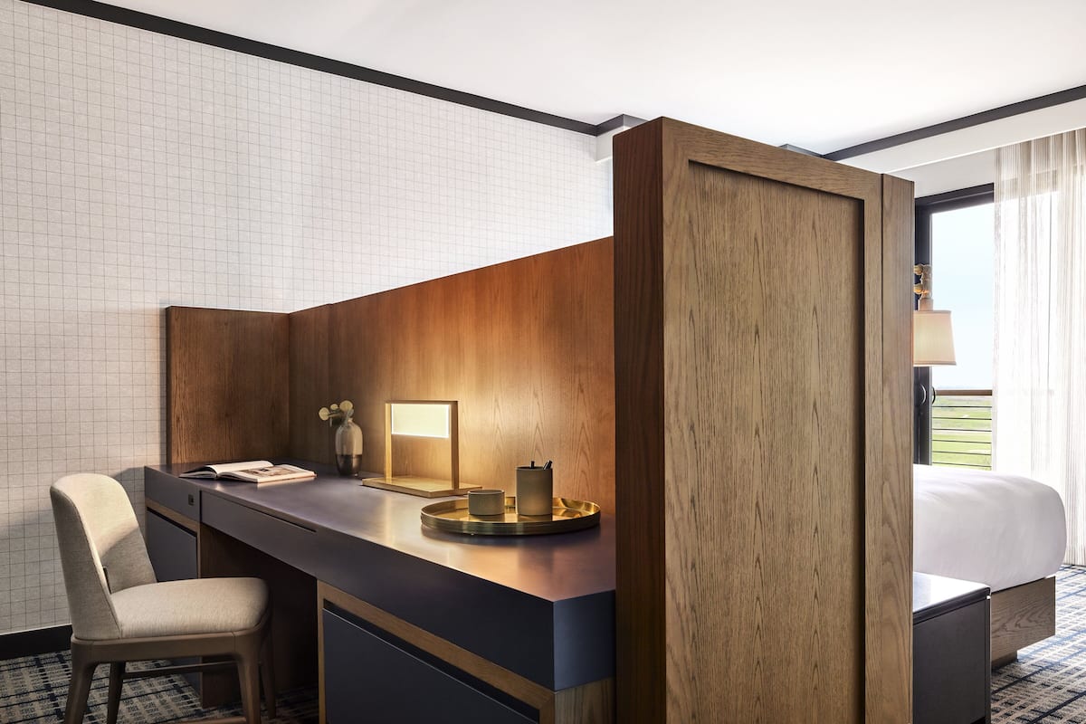 A hotel room with a desk, chair, and a bed.