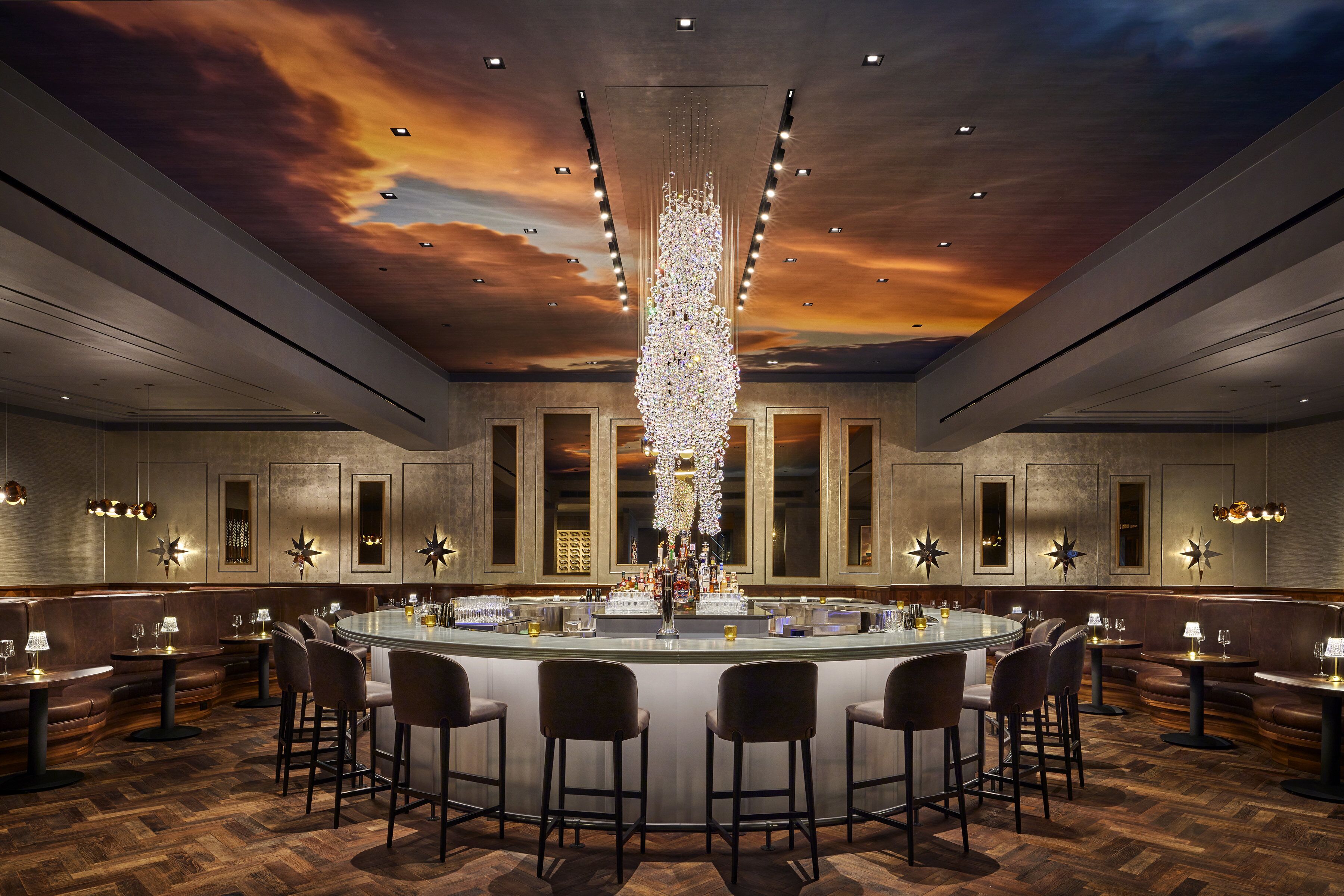 A bar area with a central bar, multiple seating options, and a ceiling with a sunset mural.