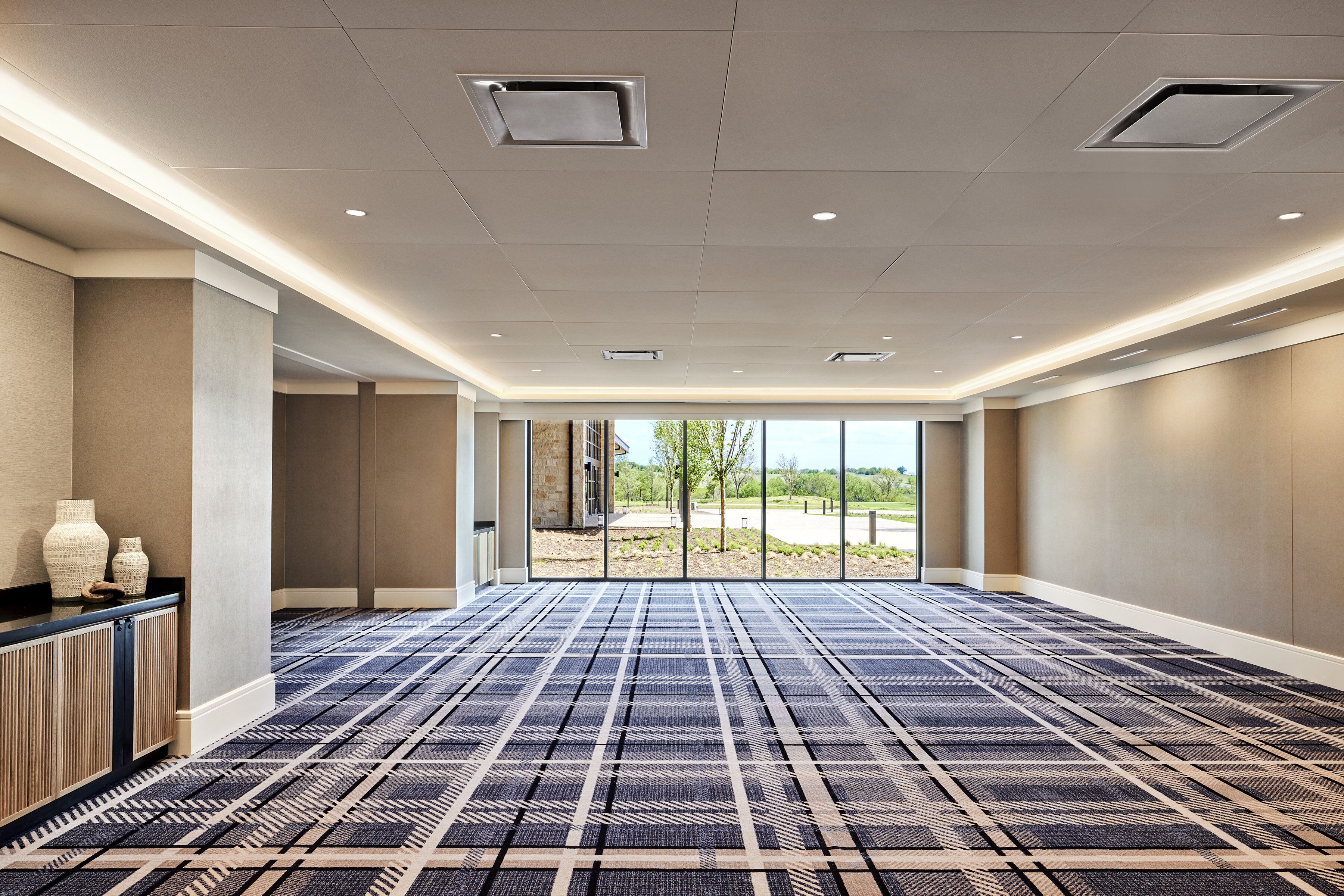Une salle de conférence spacieuse, dotée d’un tapis à motifs, d’un comptoir d’accueil et de grandes fenêtres offrant une vue sur l’extérieur.