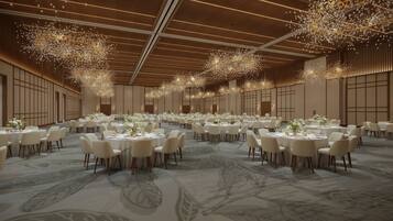 Un amplio salón de banquetes con mesas redondas, sillas blancas y elegantes candelabros.