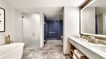 A modern bathroom with a freestanding bathtub, a large mirror, and a walk-in shower with blue tiles.