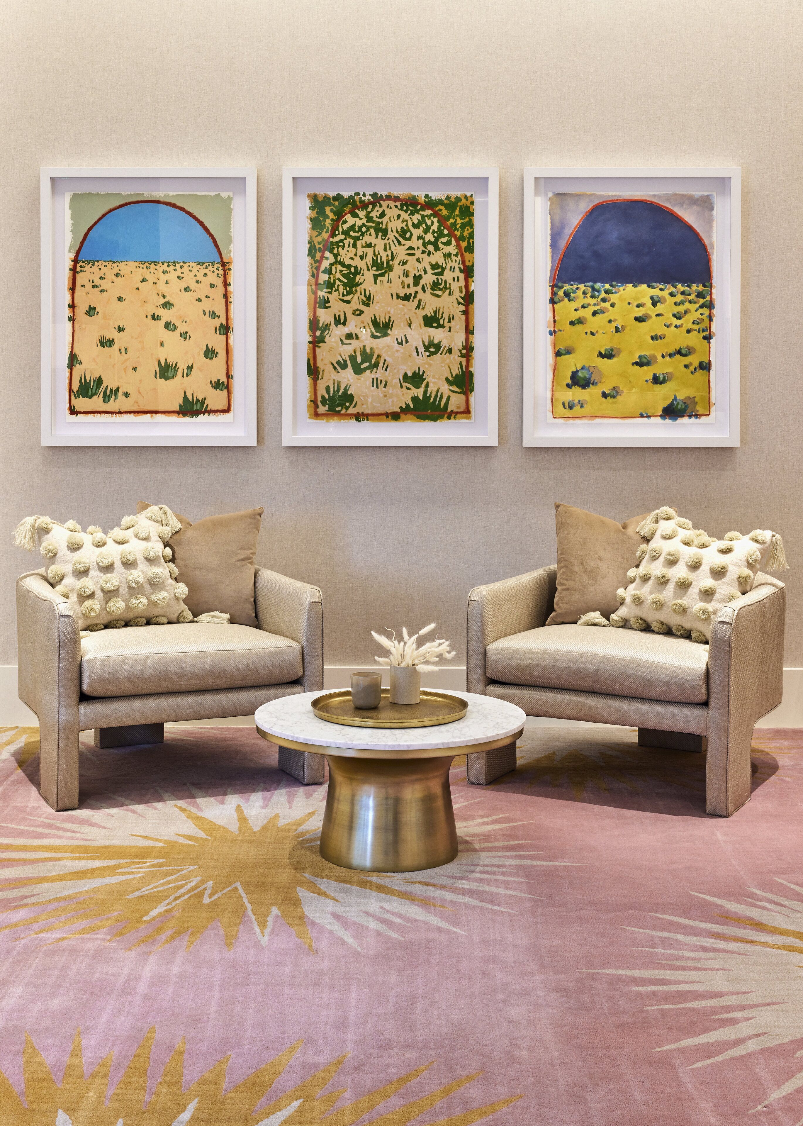 A room with two armchairs, a round coffee table, and three framed artworks on the wall.