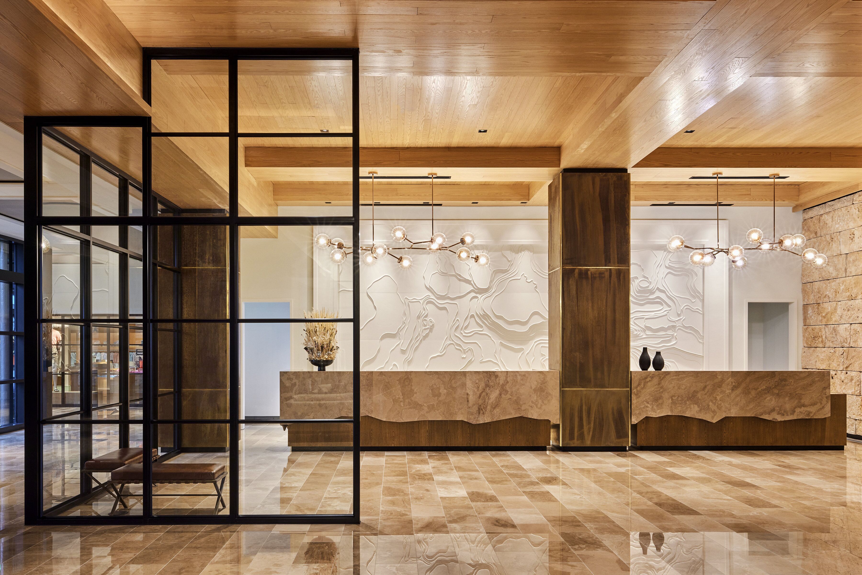 A modern lobby with a wooden ceiling, a reception desk, and a glass partition.