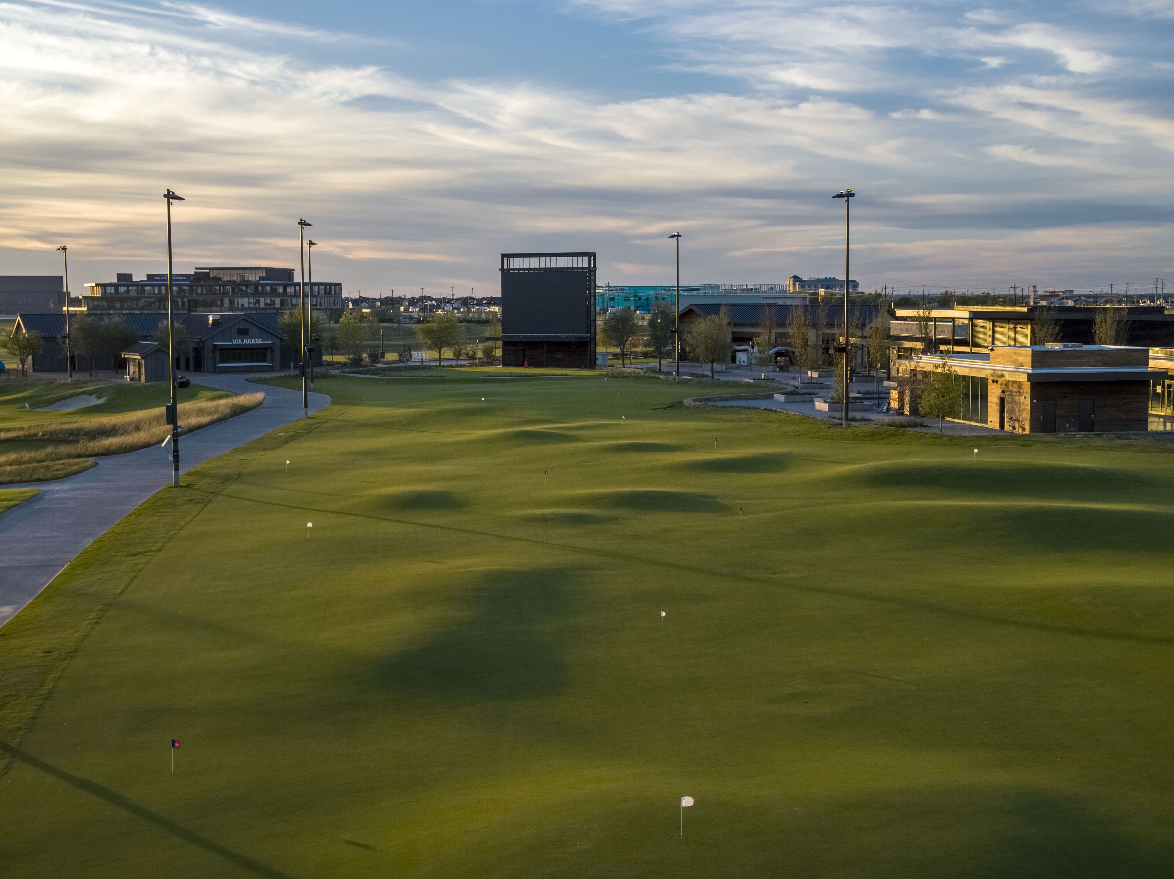 A golf course with a clear path, a building in the background, and a distant view of a city skyline.
