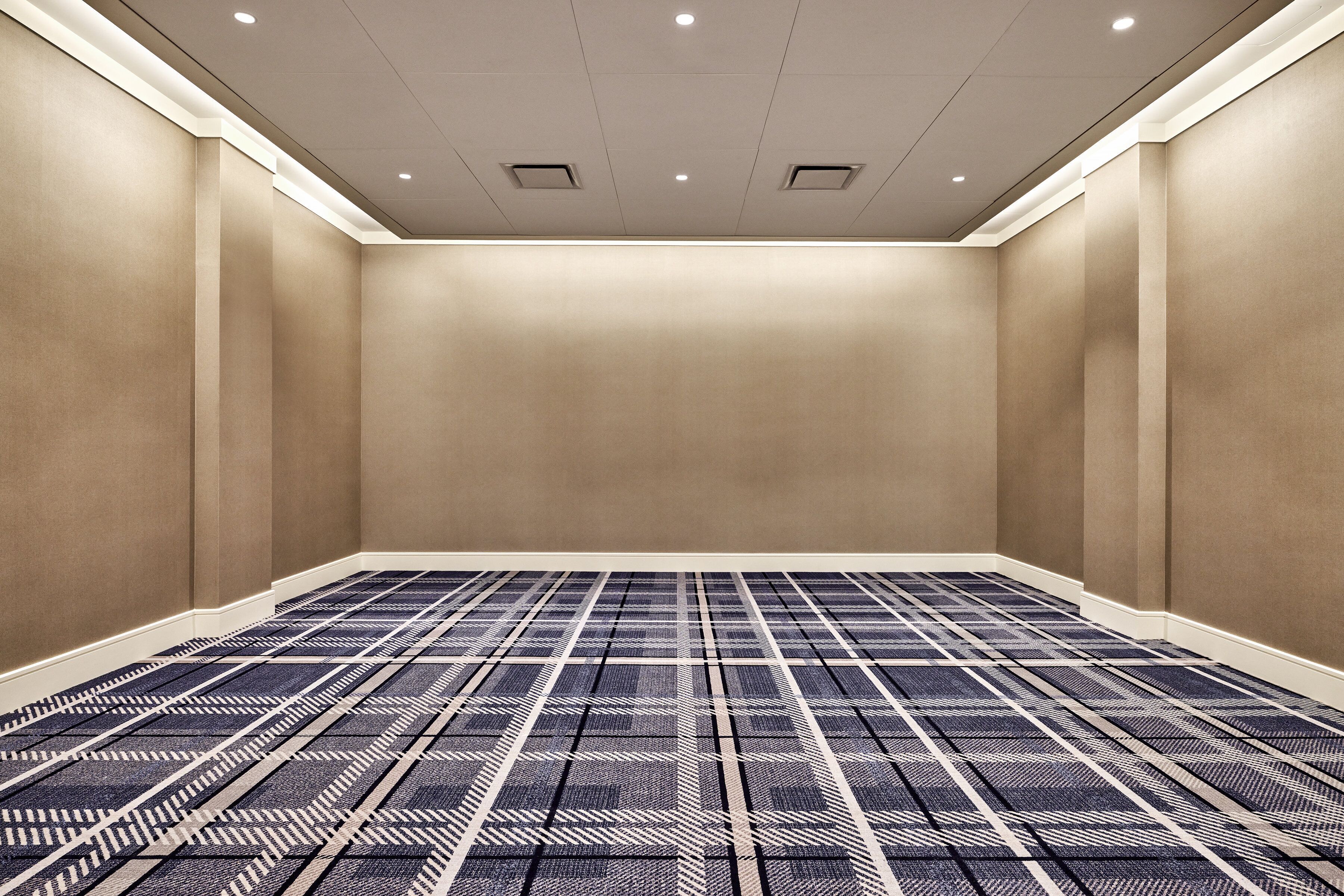 Ein Konferenzraum mit Teppichboden mit Muster, eingelassenen Deckenleuchten und beige gestrichenen Wänden.