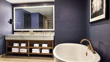 A modern bathroom with a large mirror, a bathtub, and a vanity with shelves for towels.