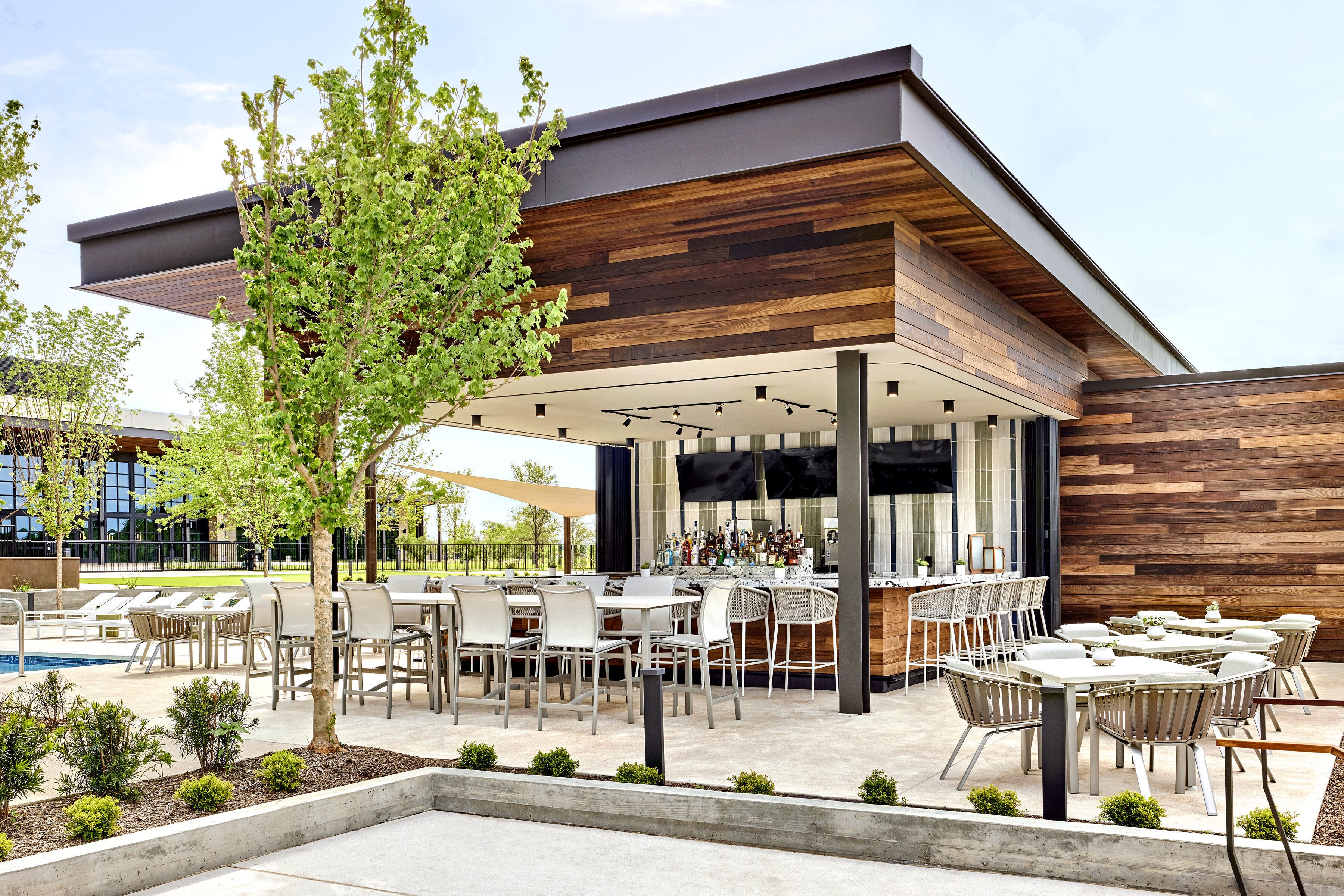 Une terrasse extérieure avec plusieurs tables et chaises, une piscine et un espace bar.