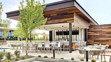 Une terrasse extérieure avec plusieurs tables et chaises, une piscine et un espace bar.