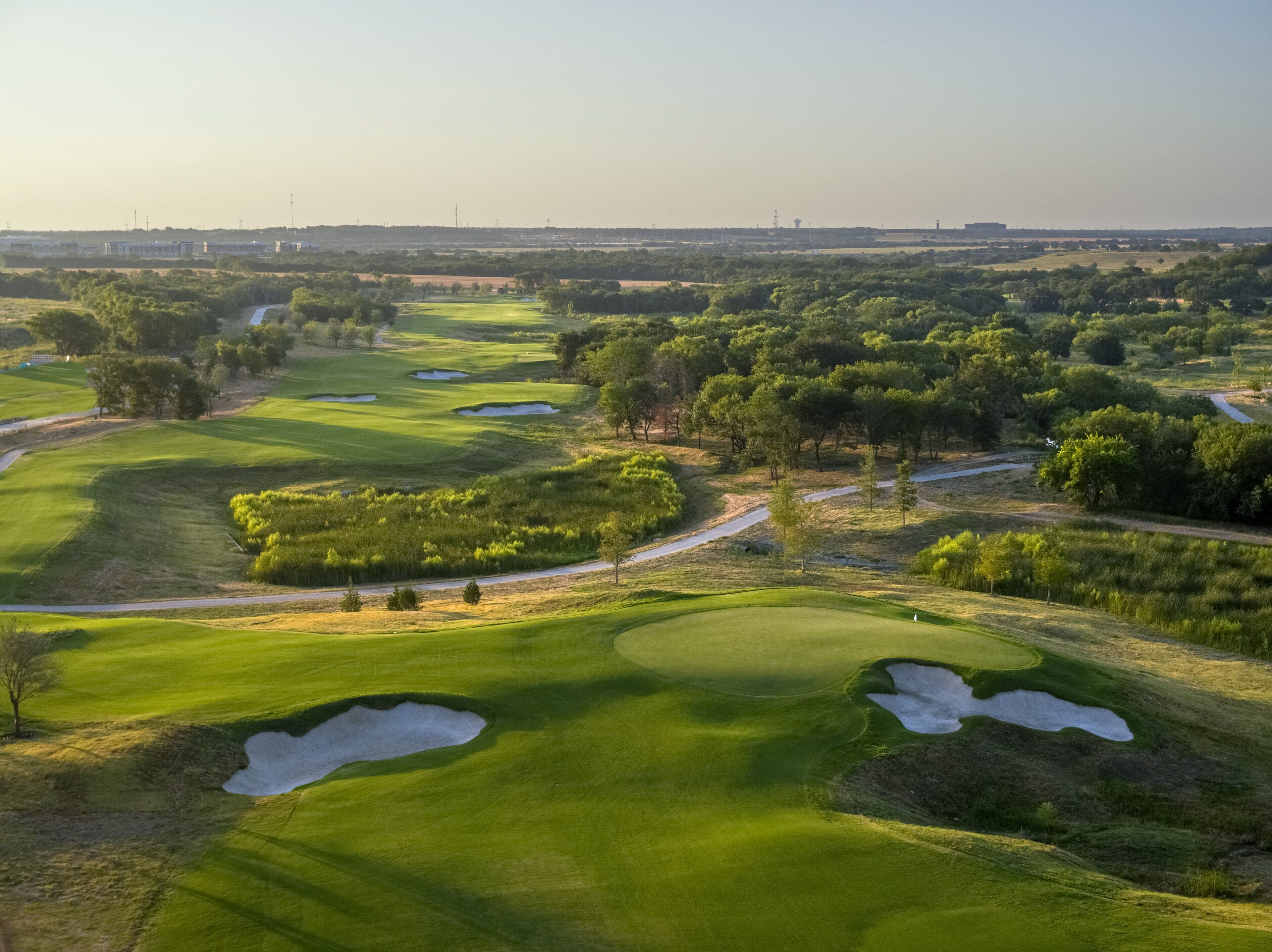 Ein Golfplatz mit mehreren Bunkern, Bäumen und blauem Himmel.