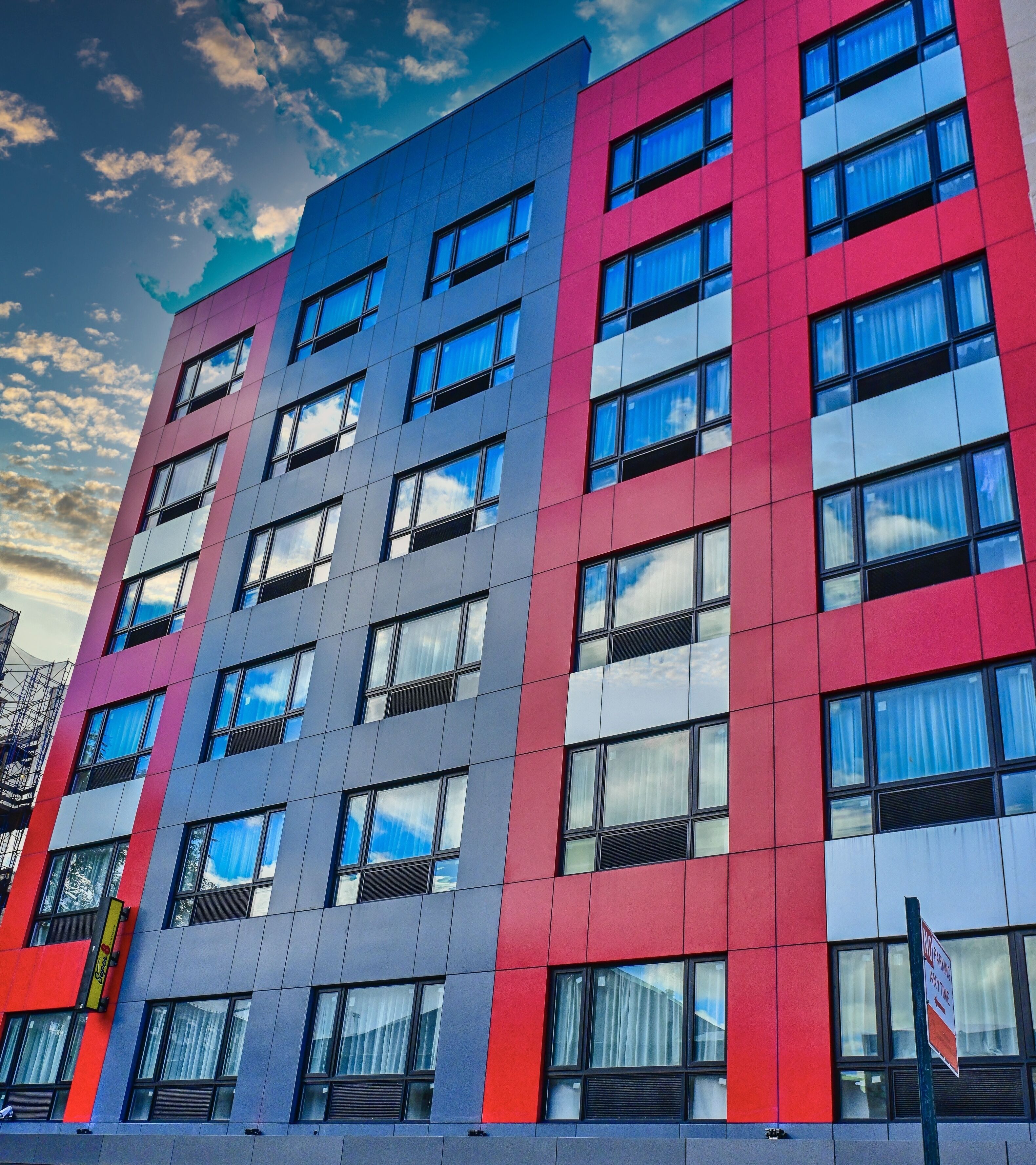 A multi-story building with a modern architectural design, featuring a combination of red, grey, and blue panels.